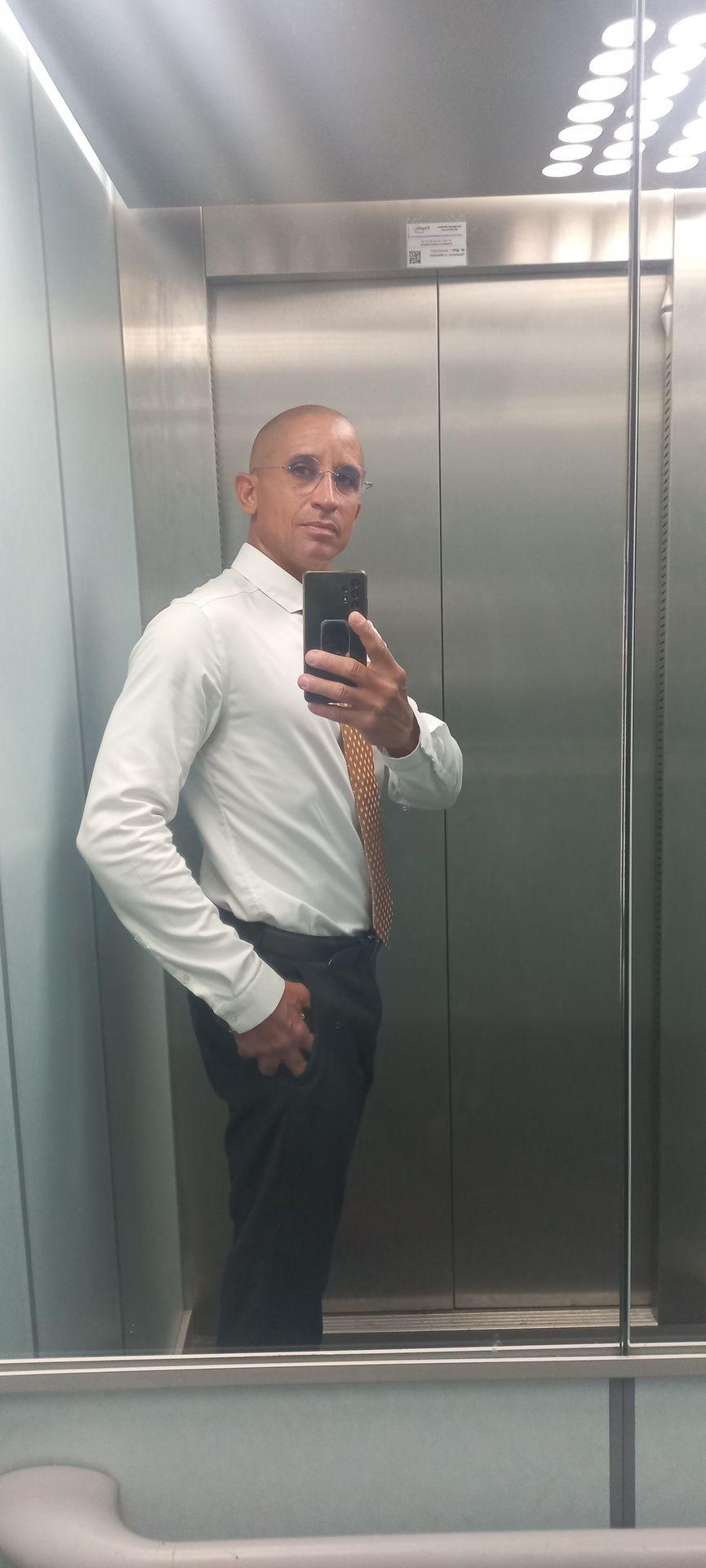 Person in white shirt and tie taking a selfie in an elevator mirror.