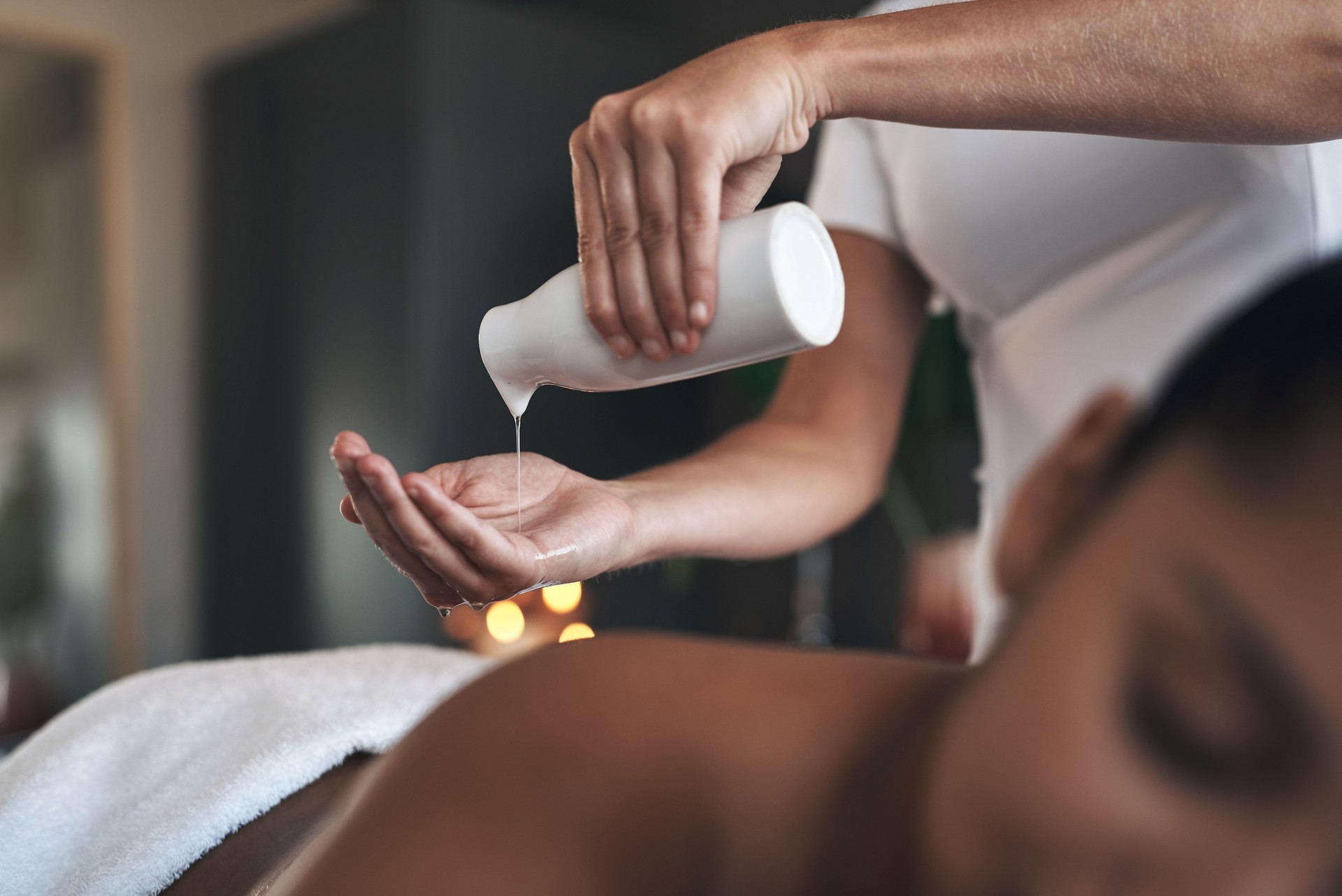 Gros plan d'un massothérapeute pressant une bouteille d'huile dans ses mains en donnant a massage à son client